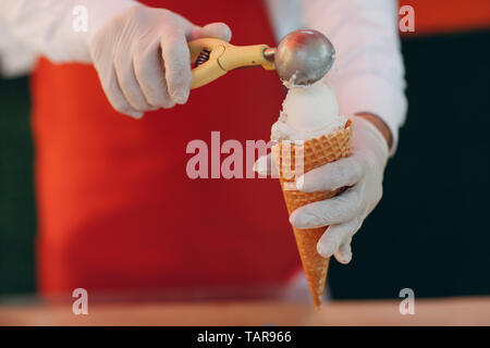 Il venditore mette il gelato in un cono di cialda Foto Stock