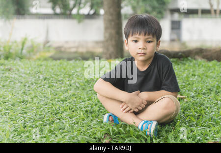 Sognante ragazzo asiatico è seduto sull'erba nel parco con spazio di copia Foto Stock