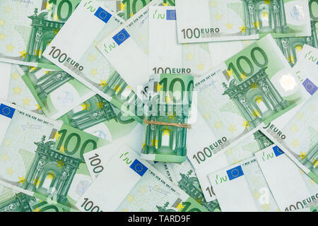 Rotolo di banconote in euro, molte banconote di 100 Euro, la moneta europea sullo sfondo. Foto Stock