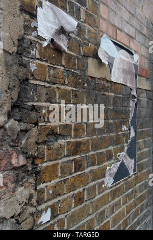 Diminuire in prospettiva di un esposto weathered muro di mattoni con strappato manifesti di strada. Foto Stock