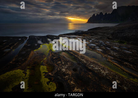 Tugeneset costa rocciosa con le montagne sullo sfondo al tramonto, Norvegia Foto Stock