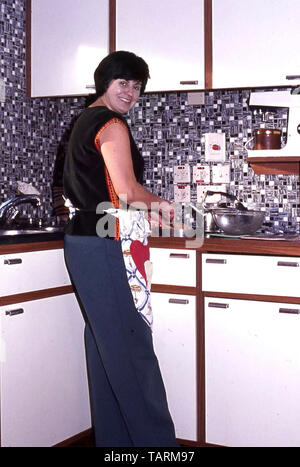 Vista Archiviazione dei giovani casalinga che prepara il cibo nel nuovo 1968 cucina DIY interno con piani di lavoro di Formica mosaico Piastrellatura murale & food mixer England Regno Unito Foto Stock