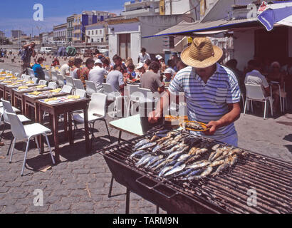 Primo piano storico 1985 urbano portoghese archivio vista di uomo lavorando alla cucina barbecue pesce sardine e servire il cibo a. gruppi di 1980 vacanza turistica persone che mangiano all'aperto Stile ai tavoli da caffè all'aperto sulla soleggiata pesca Portimao Porto e banchina in Algarve Portogallo in 'il modo in cui noi immagine degli anni '80 Foto Stock