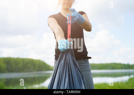 Immagine della donna nei guanti di gomma con operazione completa di Garbage Bag sulla banca del fiume in estate Foto Stock