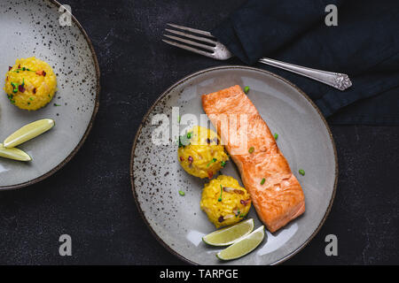 Grigliata di filetti di salmone con risotto allo zafferano e calce su sfondo scuro Foto Stock