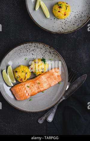 Grigliata di filetti di salmone con risotto allo zafferano e calce su sfondo scuro Foto Stock