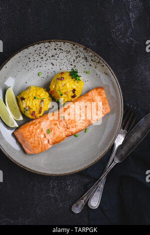 Grigliata di filetti di salmone con risotto allo zafferano e calce su sfondo scuro Foto Stock