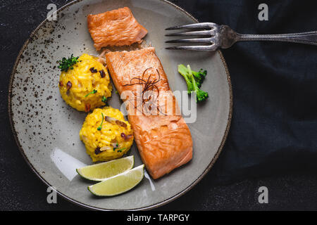 Grigliata di filetti di salmone con risotto allo zafferano e calce su sfondo scuro Foto Stock