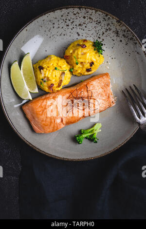 Grigliata di filetti di salmone con risotto allo zafferano e calce su sfondo scuro Foto Stock