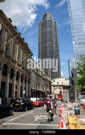 Una vista su Bishopsgate a Londra. I ciclisti di competere con il traffico in primo piano mentre la torre 42, un moderno grattacielo, si eleva alto in background. Foto Stock