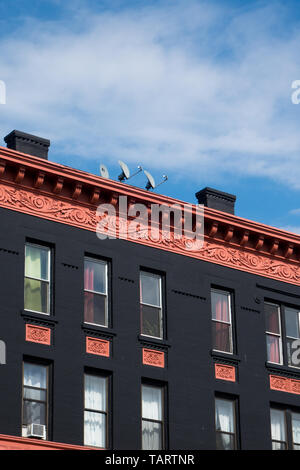 La ornata di ornamentazione architettonica sulla parte superiore di un colorato il vecchio edificio in Brooklyn, New York, USA, contro un cielo blu. Foto Stock