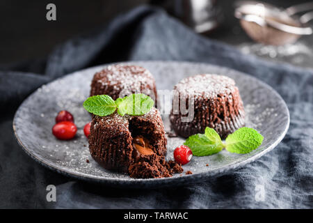 La Lava torte al cioccolato decorato con foglia di menta e bacche rosse sulla piastra. Cibo scuro foto. Gustosi dessert al cioccolato Foto Stock