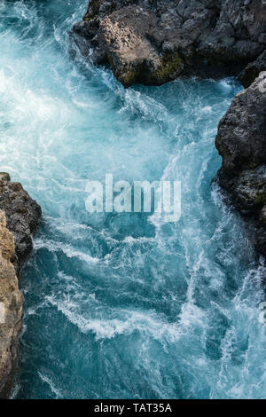 Il blu ghiaccio acqua del fiume Hvítá versando sopra la cascata di Barnafoss in occidente in Islanda, tra le scogliere di lava nera Foto Stock
