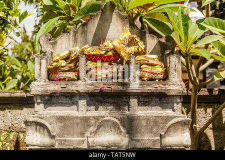 Tripla altare in pietra dedicato alla Trimurti - Brahma, Shiva e Vishnu con indù tradizionali offerte Balinese canang sari. Bali, Indonesia. Foto Stock