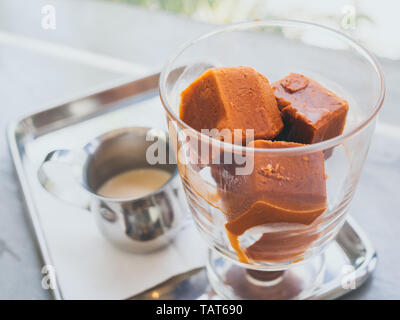 Thai tè latte di cubetti di ghiaccio nel bicchiere con il latte nel bricco di piccole dimensioni sul vassoio in acciaio inox su cemento tabella. Foto Stock