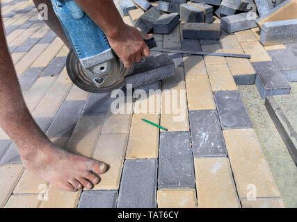 Il lavoratore effettua il taglio di una barra della pavimentazione in lastre per la posa finale sulla terrazza su una strada di città a mezzogiorno. Foto Stock