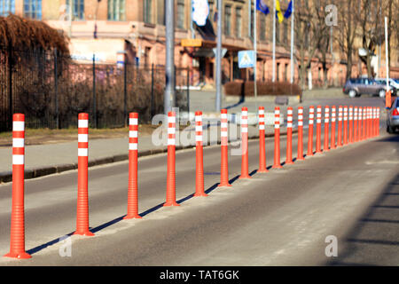 Rosso su strada riflettente colonne dividono la strada a metà contro lo sfondo di una strada di città e il parcheggio alla luce dei raggi del sole. Foto Stock