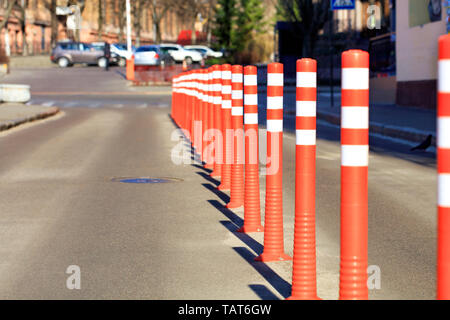 Rosso su strada riflettente colonne dividono la strada a metà tra l'entrata del parcheggio in una sfocatura nella luce del sole. Foto Stock