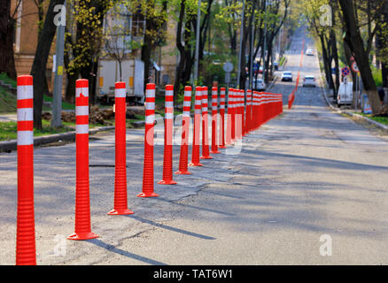 Rosso su strada riflettente colonne dividono una cattiva strada a metà contro lo sfondo di ombre e di una strada sfocata sotto i raggi del sole. Foto Stock