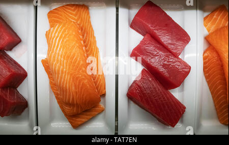 Diversi grandi pezzi di tonno e salmone per sushi giacciono su una piastra bianca nel banco frigo. Foto Stock