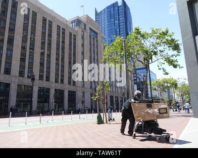 San Francisco, Stati Uniti d'America. Il 10 maggio, 2019. Un senzatetto guy spinge un carrello della spesa con le sue cose lungo la strada del mercato. Il quartier generale di Twitter è in background. Il tech boom di San Francisco e la vicina Valle di silicio ha fornito la regione con decine di migliaia di posti di lavoro e molti nuovi milionari. Il lato negativo: esplosione di affitti e dei senzatetto per le strade. La vita in questo profondamente diviso la città diventa inestimabile. (A dpa 'miliardari e povertà: la grande tech quake divide San Francisco' dal 26.05.2019) Credito: Barbara Munker/dpa/Alamy Live News Foto Stock