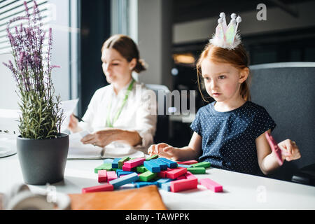 Imprenditrice con figlia piccola seduta in un ufficio, lavorando. Foto Stock