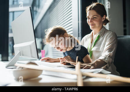 Imprenditrice con figlia piccola seduta in un ufficio, lavorando. Foto Stock