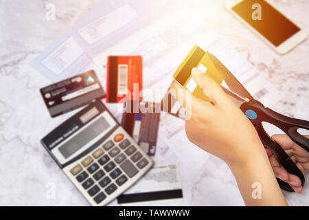 Le donne usano le forbici per tagliare le carte di credito in mano con molte carte di credito e di dichiarazione sulla tabella per lo sfondo Foto Stock