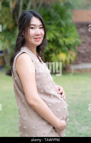 Asian bella donna incinta di riposo in giardino sfondo. Foto Stock