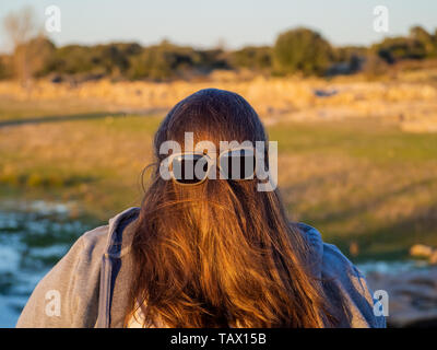 Una curva donna fare gesti divertenti con i capelli davanti al suo volto e occhiali da sole Foto Stock