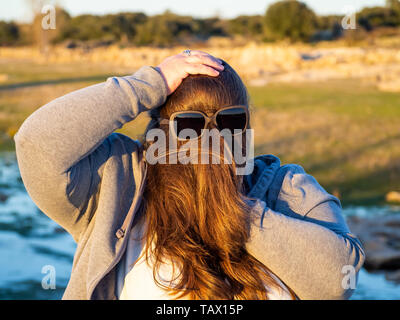 Una curva donna fare gesti divertenti con i capelli davanti al suo volto e occhiali da sole Foto Stock