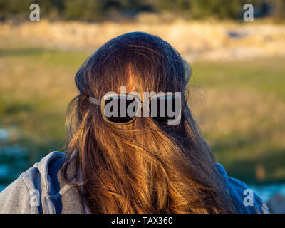 Una curva donna fare gesti divertenti con i capelli davanti al suo volto e occhiali da sole Foto Stock