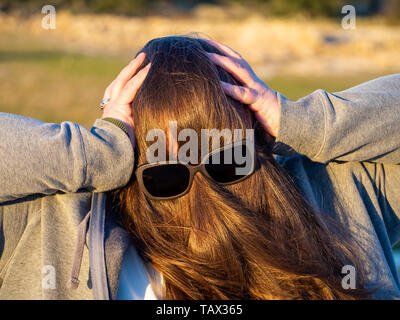 Una curva donna fare gesti divertenti con i capelli davanti al suo volto e occhiali da sole Foto Stock