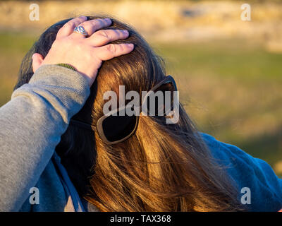Una curva donna fare gesti divertenti con i capelli davanti al suo volto e occhiali da sole Foto Stock