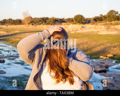 Una curva donna fare gesti divertenti con i capelli davanti al suo volto e occhiali da sole Foto Stock