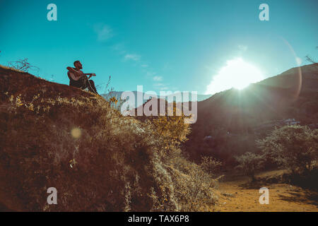 Uomo a suonare la chitarra sulle montagne Foto Stock