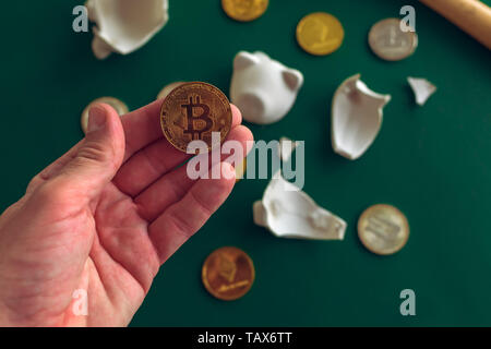 Tenendo la mano Bitcoin da broken piggy coin bank, cryptocurrency concetto di risparmio. Foto Stock