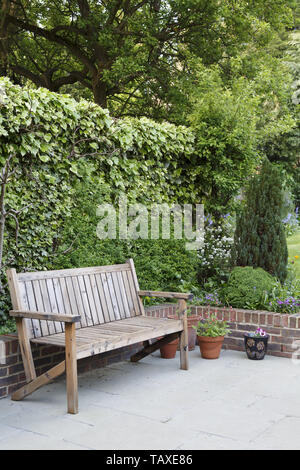 Giardino in legno panca su un patio in un tipico quartiere periferico di giardino sul retro in Londra, Regno Unito Foto Stock