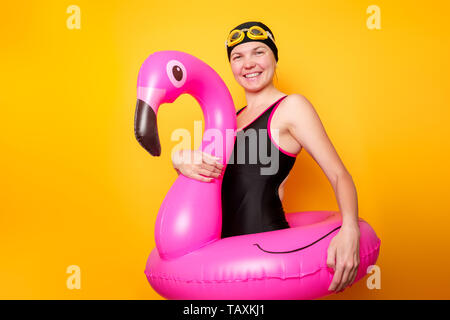 Immagine di donna in costume nero con flamingo salvagente su vuoto sfondo arancione Foto Stock