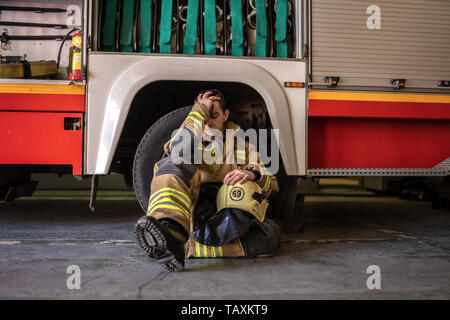 Immagine di stanchi fireman seduto sul pavimento vicino al camion dei pompieri Foto Stock