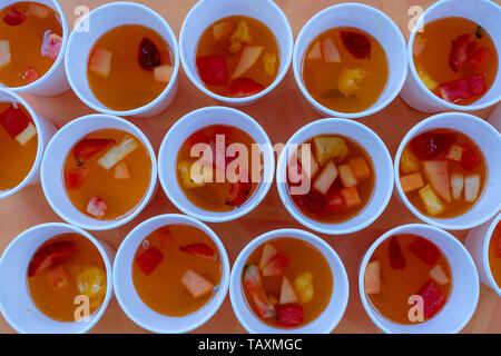 Un sacco di frutta dolce limonata dal rosso di fragole, meloni e ananassi in una in bianco tazze . Close up. Bevanda rinfrescante da pezzi di frutta, top vie Foto Stock