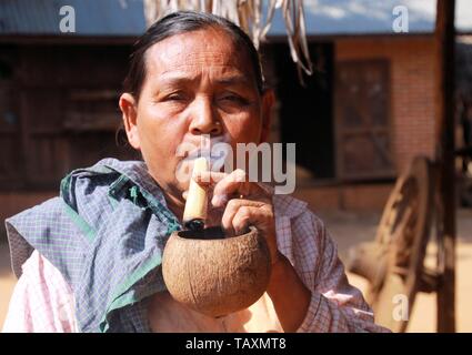 BAGAN, MYANMAR - Dicembre 21. 2015: ritratto della vecchia età donna birmano fumare una self made sigaro tradizionale utilizzando un guscio di noce di cocco come portacenere Foto Stock