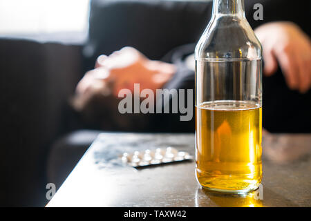 Uomo ubriaco con alcool bere e pillole sul tavolo di dormire sul lettino Foto Stock