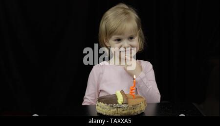 Piccola ragazza carina la realizzazione di un desiderio prima di soffiare festosa candela sulla torta di compleanno. Felice 4 anni bambino. Dolce, cute capelli biondi ragazza Foto Stock