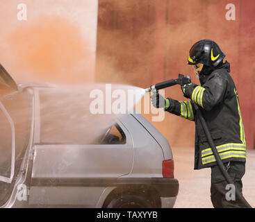 Vigile del fuoco con il casco utilizza schiuma durante un incidente stradale sulla vettura rotto Foto Stock