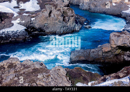 Blu, fiume torrenziale circondata da rocce laviche in inverno di Islanda Foto Stock