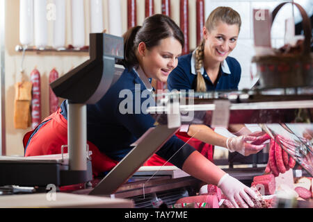 Due donne di vendite nel negozio di macellaio ripieno il display di carne Foto Stock