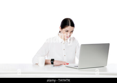 Ritratto di attenta gravi attraente brunette imprenditrice in camicia bianca seduto con laptop e guardando il display e leggendo qualcosa. indoo Foto Stock