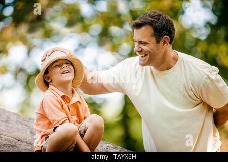 Padre sorridente scherzosamente collocando un cappello di paglia sul suo figlio di testa. Foto Stock