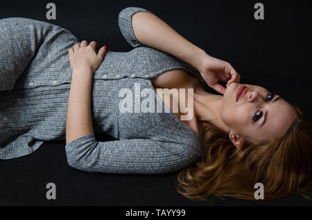 Ragazza Shapely dalla Polonia. Giovani modello femminile in posa di studio con sfondo nero. Bella ragazza in abito grigio posa sulla terra. Foto Stock